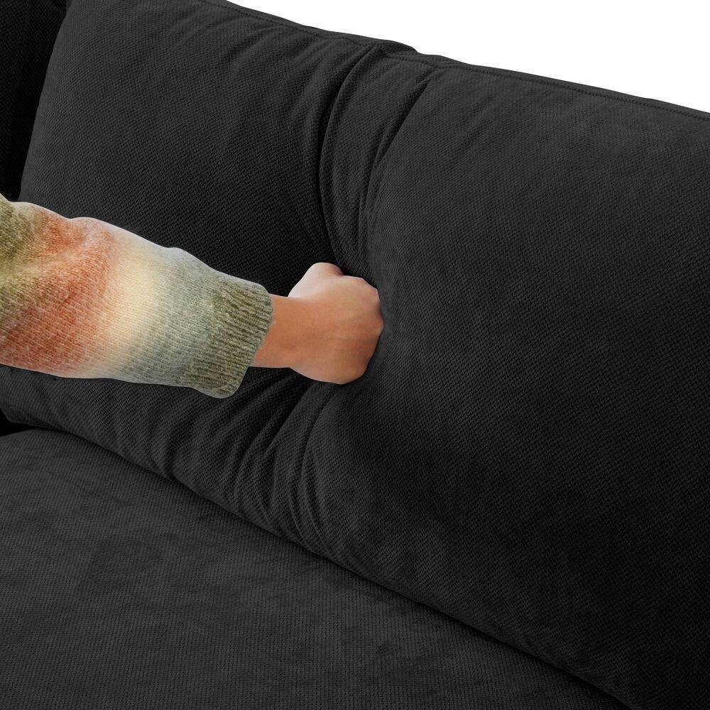 Close-up of a hand pressing into a black linen sofa cushion.