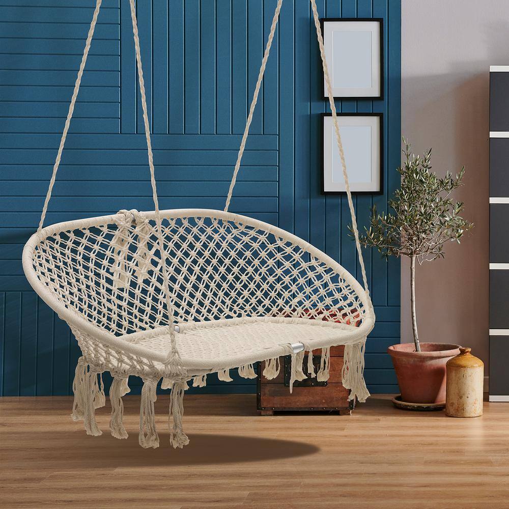 A cream white macramé hanging hammock chair in an indoor room.
