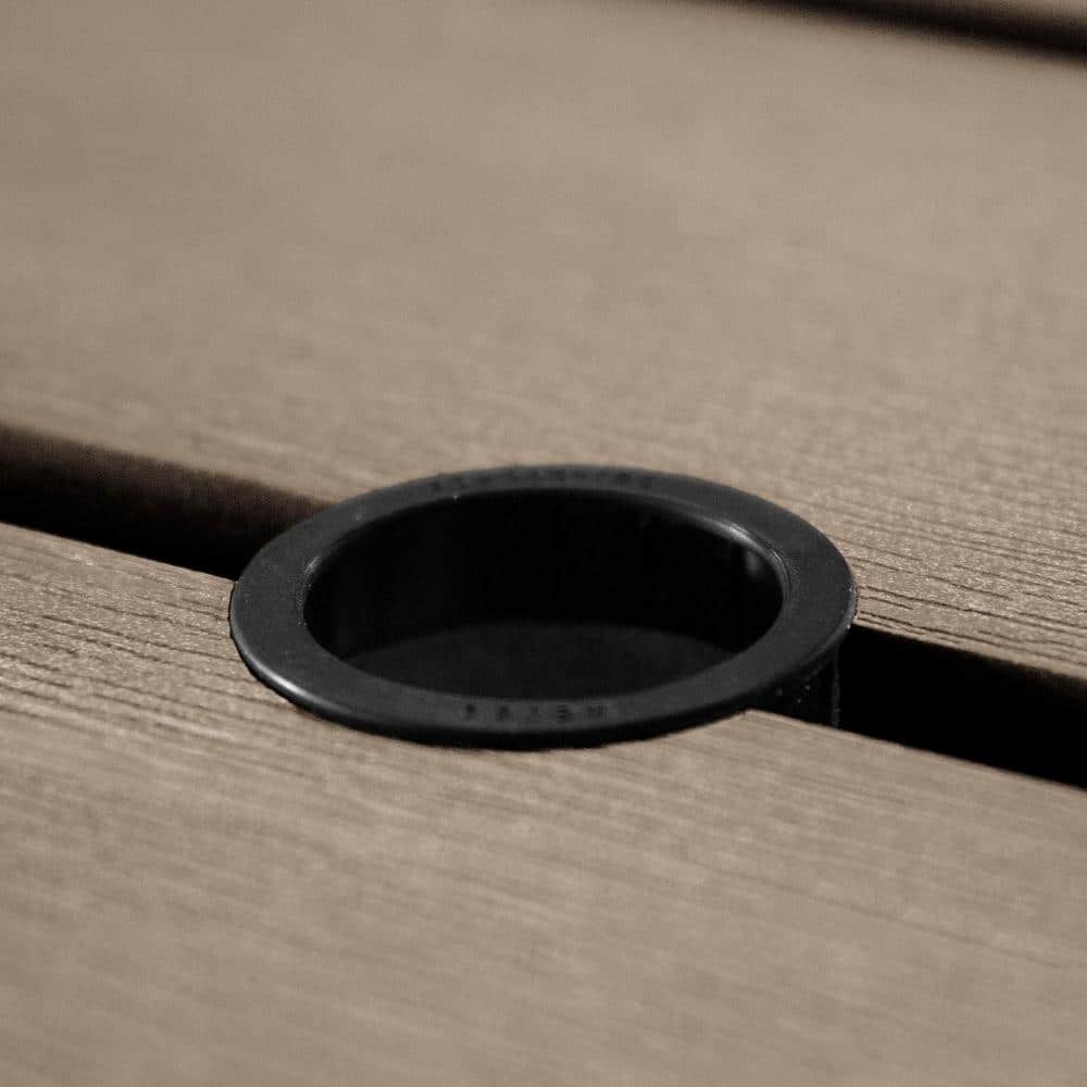 A close-up of a black circular umbrella hole in a tan picnic table.