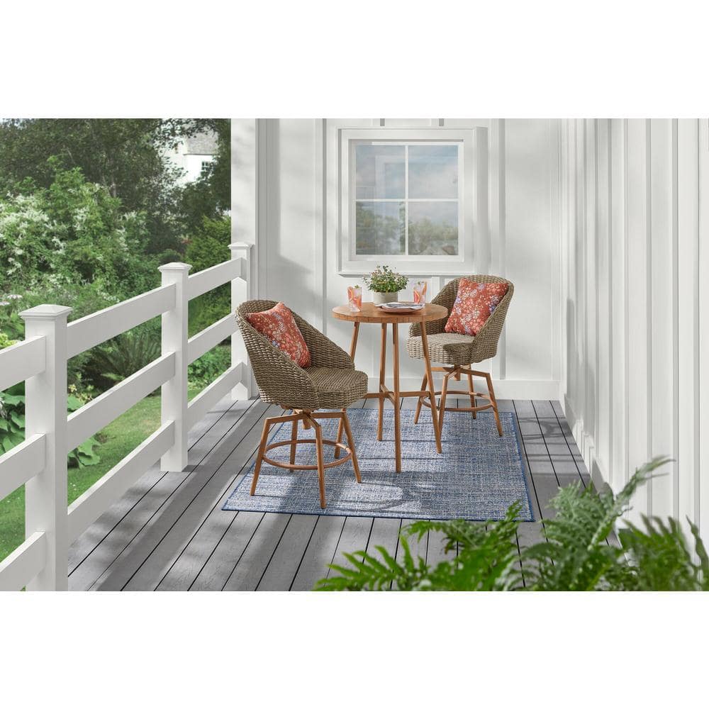 Wicker dining set with a round table and pillows on an outdoor deck.