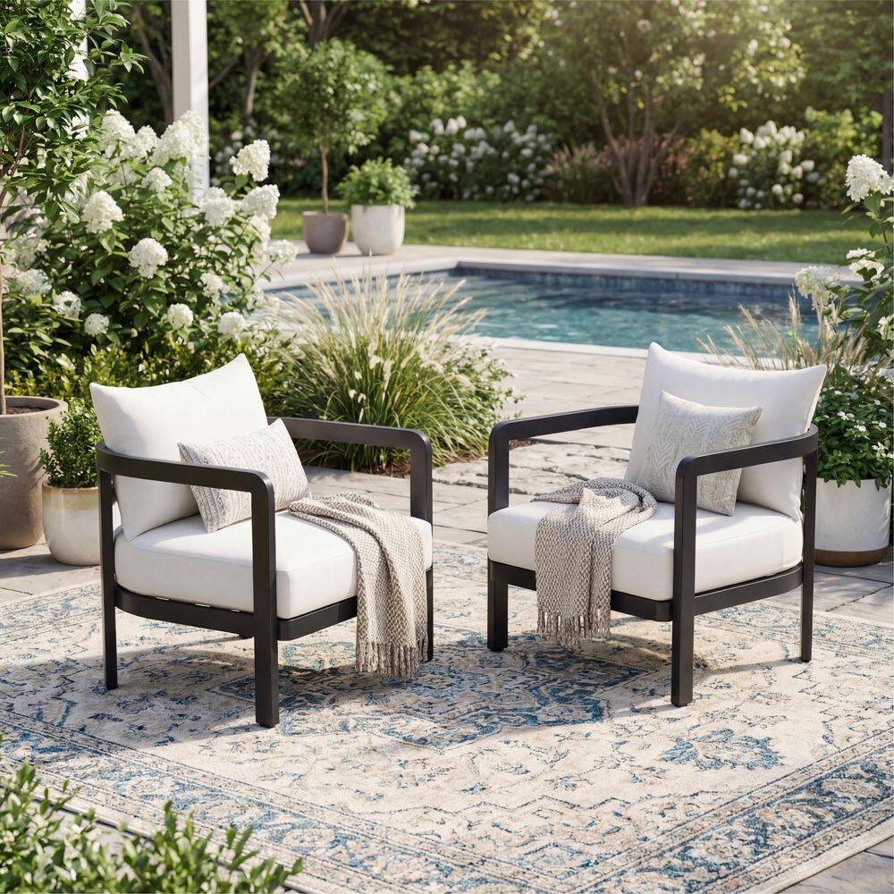 Two black outdoor club chairs with white cushions and decorative pillows in a garden setting.