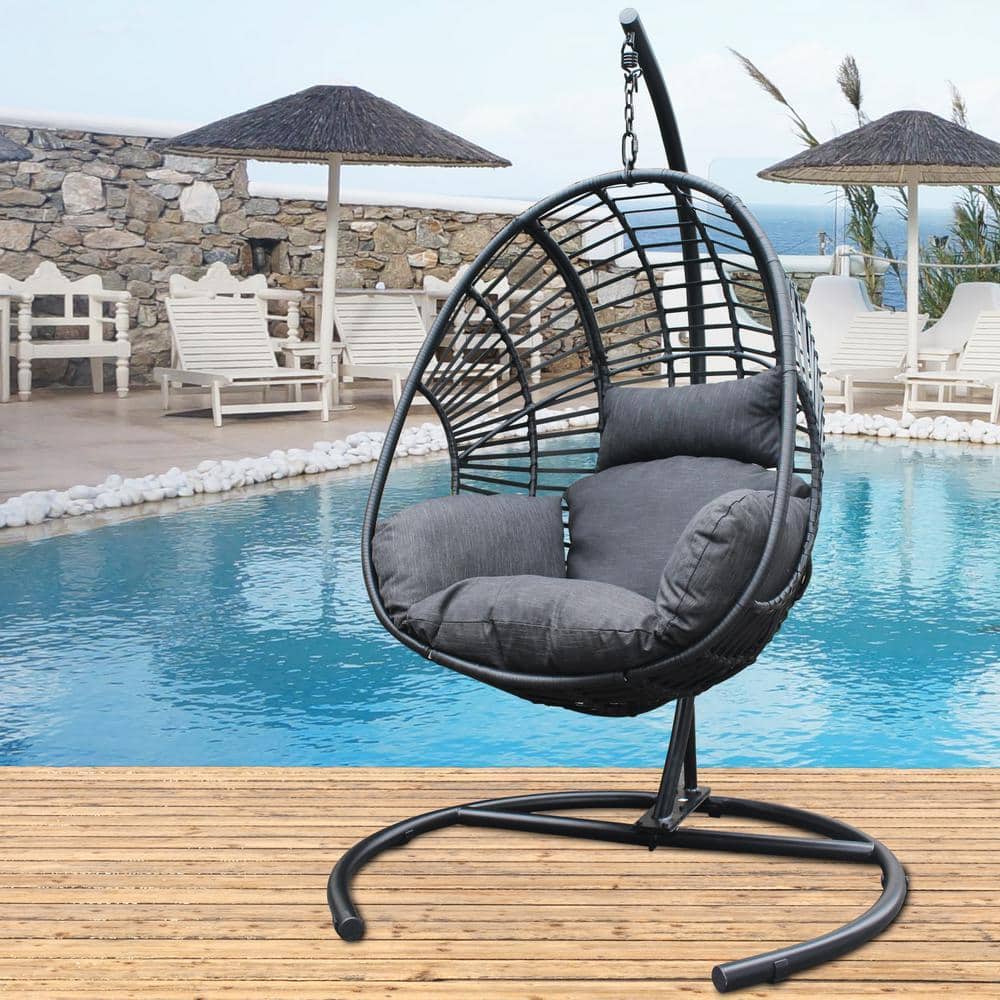 Black wicker swing egg chair with anthracite cushions by a pool.