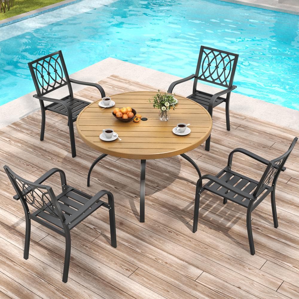 Outdoor dining set with round wood-grain table and four black metal chairs by a pool.