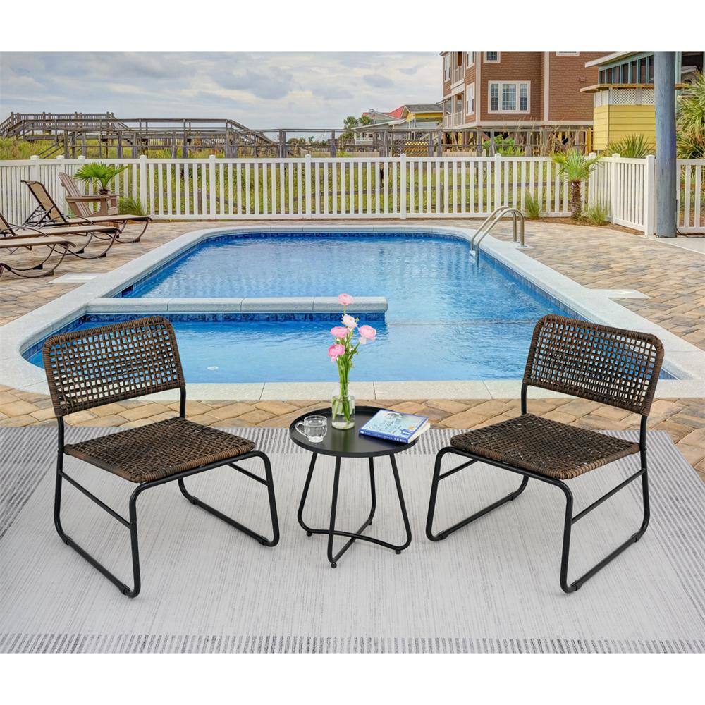 Two brown wicker patio chairs and a black round table set by a swimming pool.