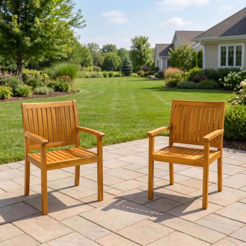Two acacia wood outdoor dining chairs on a stone patio overlooking a lawn.