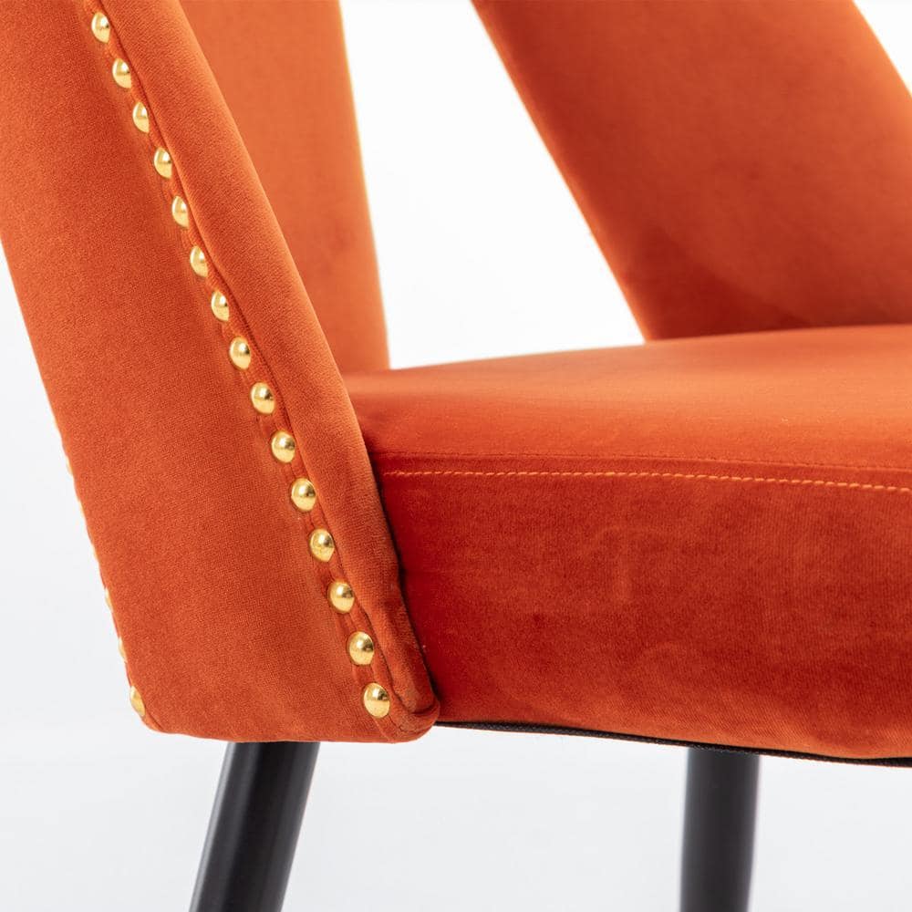 Close-up of the gold nailhead trim on the side of an orange velvet chair.